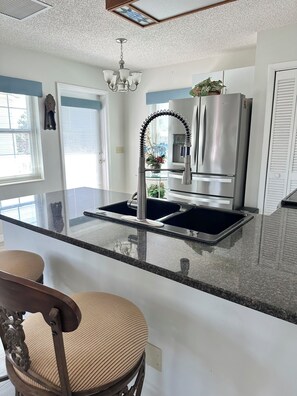 A modern kitchen with a central island, stainless steel appliances, and a decorative chandelier. - Hammock Beach Cottage (Palm Coast)