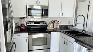 A modern kitchen with stainless steel appliances, white cabinetry, and a granite countertop. - Hammock Beach Cottage (Palm Coast)