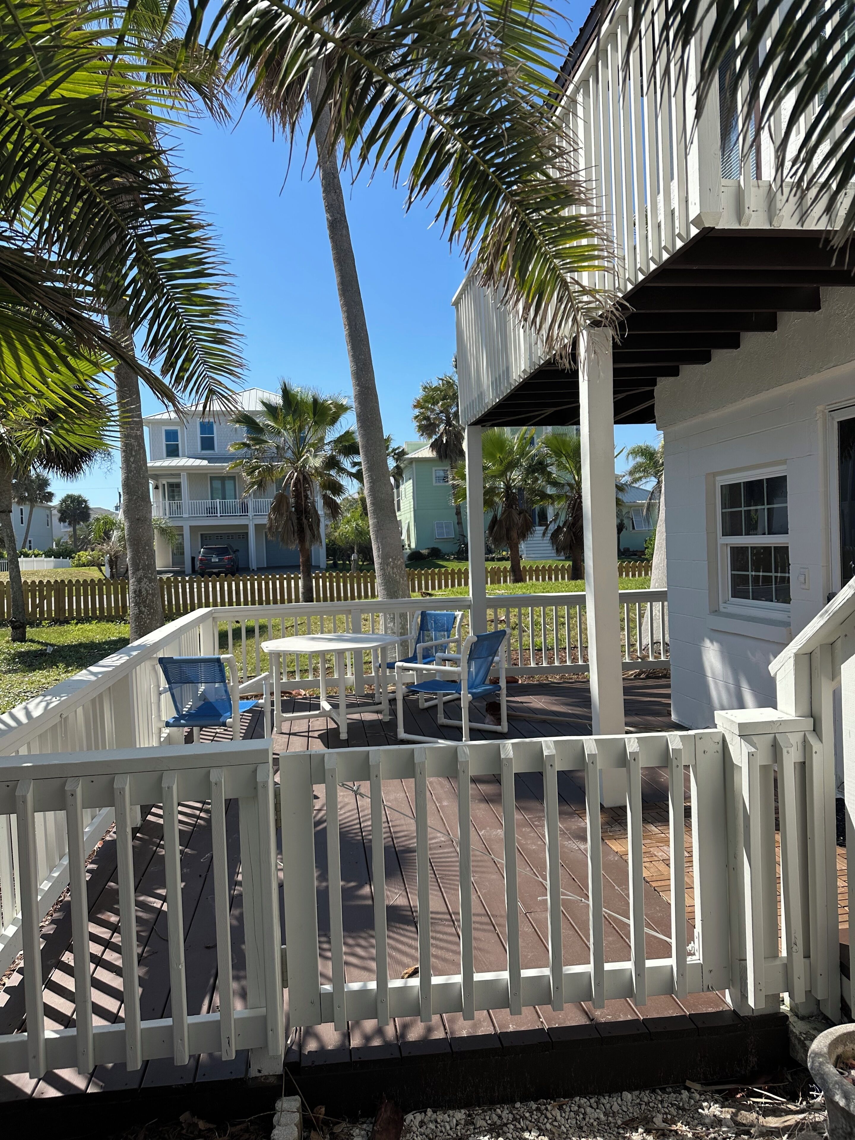 A wooden deck with white railings, blue chairs, and a small table.
