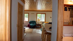Ein Zimmer mit Holzbalkendecke, einem Esstisch mit Barhocker, einem roten Stuhl und einer Lampe.