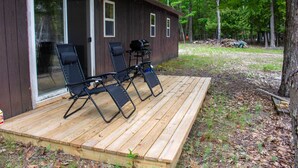 Eine Holzterrasse mit vier Liegestühlen und einem Grill.