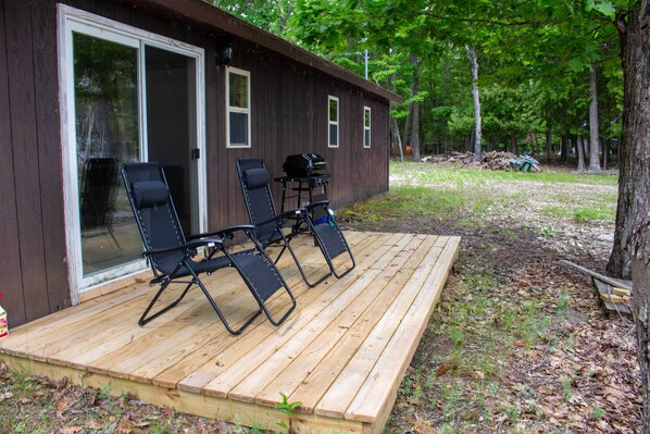 Eine Holzterrasse mit vier Liegestühlen und einem Grill.