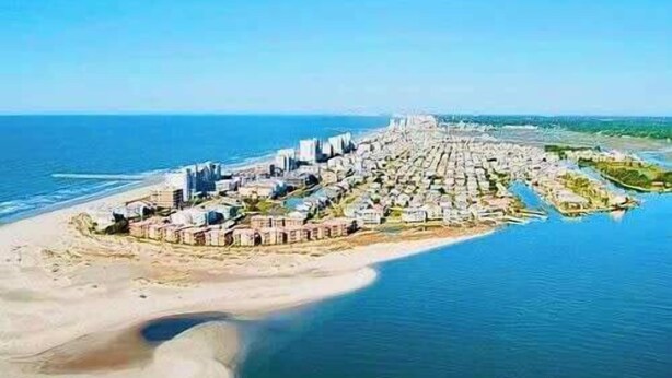 An aerial view of a coastal resort with beachfront villas, a marina, and a central building likely serving as a hotel or resort center.