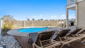 A backyard with a swimming pool, lounge chairs, and a wooden deck.