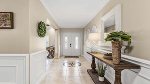 Un pasillo con una puerta blanca, una consola de madera con una planta y un espejo en la pared.