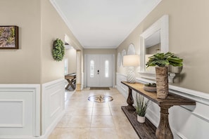 A hallway with a white door, a wooden console table with a plant, and a mirror on the wall.