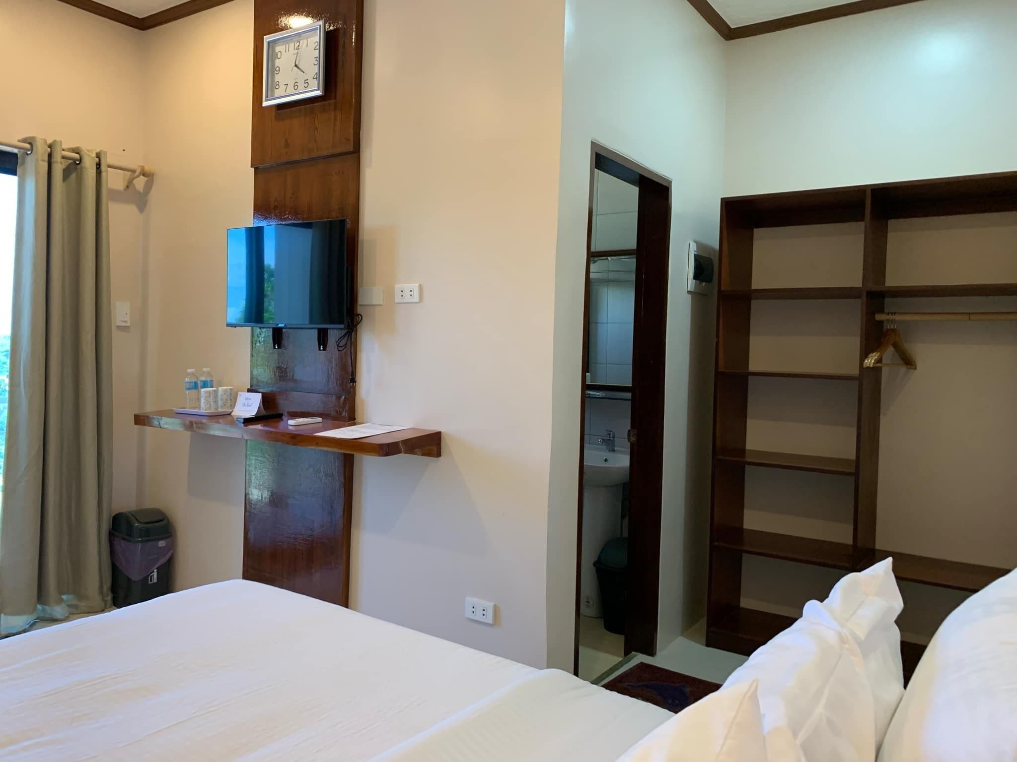 Une chambre d’hôtel avec un lit, un téléviseur fixé sur une étagère en bois, un miroir et une armoire.