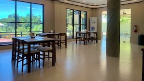 Àrea interior espaiosa amb grans finestres, taules i cadires de fusta.
