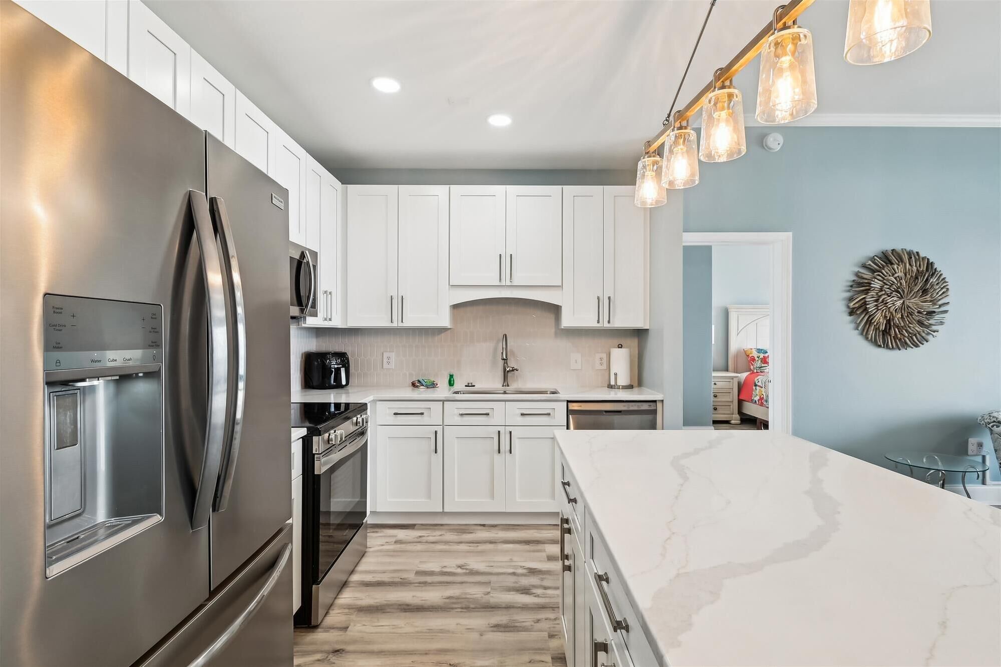 A modern kitchen with white cabinets, stainless steel appliances, and a marble countertop.