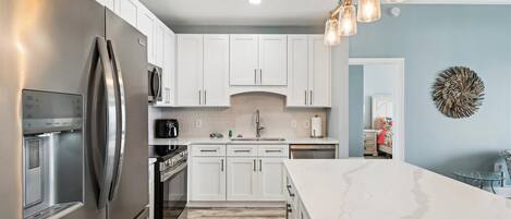 A modern kitchen with white cabinets, stainless steel appliances, and a marble countertop.