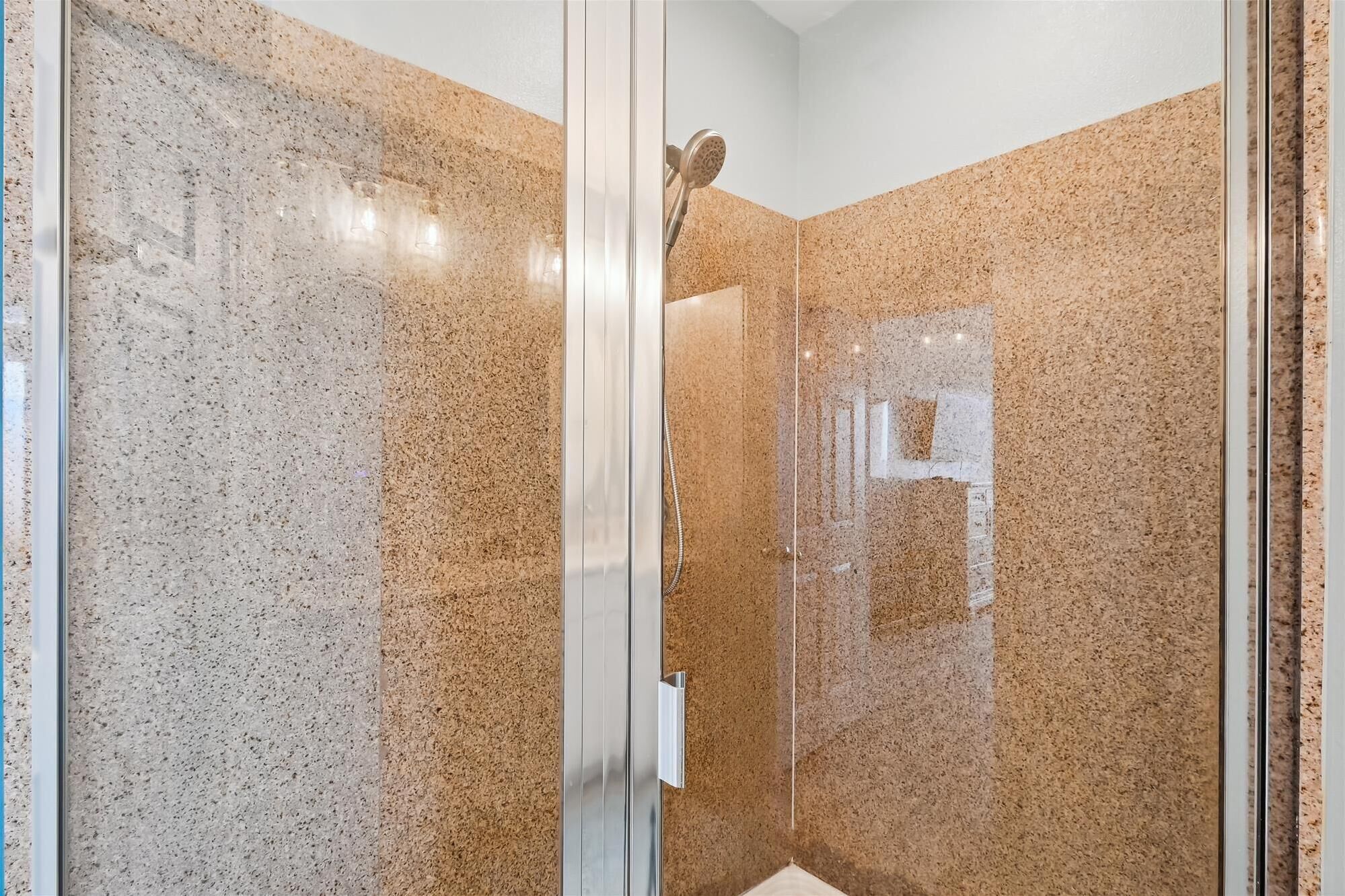 Une douche fermée par des parois de verre avec un mur en granit.