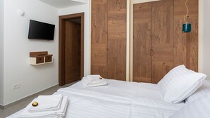 Un dormitorio con cama, armario de madera, televisor montado y estante con toallas.