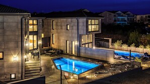 Un edificio moderno con piscina, mobiliario exterior y una escalera que conduce a la entrada.