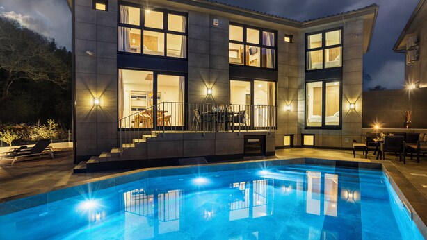 Una casa moderna de dos pisos con piscina, ventanas amplias y mobiliario exterior.