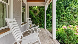 A covered porch with white wooden chairs and a table, surrounded by lush greenery and flowering plants. - Charming 6-bedroom house with AC, WiFi in wonderful West Cape May (West Cape May)