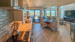 A modern kitchen with a large island, a dining area with wicker furniture, and a stone accent wall.