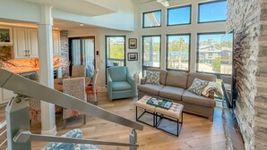 A spacious living area with a high ceiling, large windows, a staircase, and a view of the outdoors.