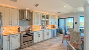 A modern kitchen with white cabinetry, a stainless steel range hood, and a large island with a marble countertop.
