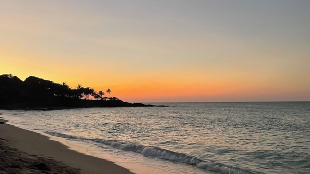 Une plage aux vagues douces et un ciel dégagé au coucher du soleil.