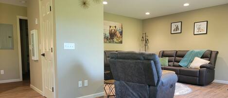 Een woonkamer met een grijze fauteuil, een bruine bank met een groene plaid en een schilderij van een beer aan de muur.