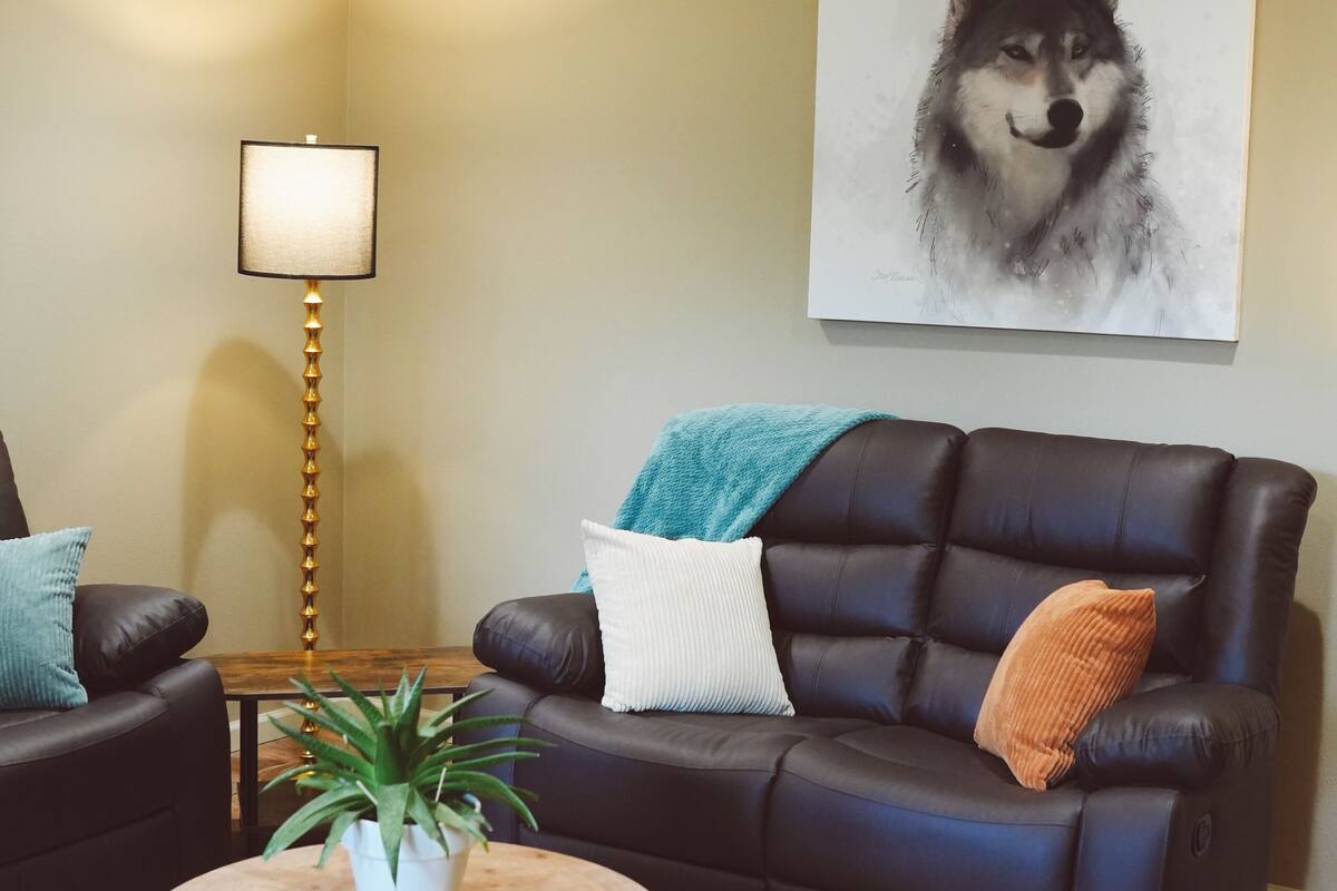 A living room with a dark leather sofa, a round wooden coffee table, a floor lamp, and a large painting of a dog on the wall.