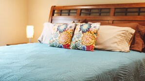 A bed with a floral-patterned pillow and a plain pillow, a wooden headboard, and a nightstand with a lamp. - Sprucewood Dens (Homer)