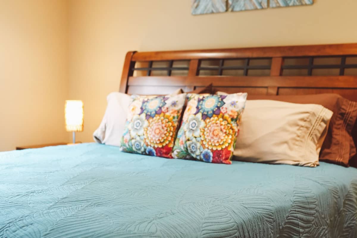 A bed with a floral-patterned pillow and a plain pillow, a wooden headboard, and a nightstand with a lamp.