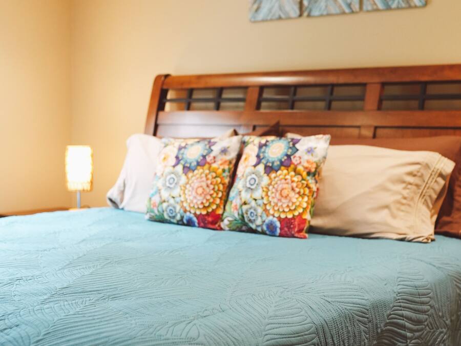 Uma cama com um travesseiro estampado com flores, um travesseiro liso, uma cabeceira de madeira e uma mesa de cabeceira com abajur.