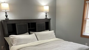 Une chambre à coucher avec un cadre de lit en bois foncé, deux oreillers blancs, une couvre-lit beige et deux lampes de chevet.