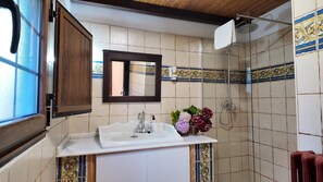 A bathroom with a white sink, a mirror, a shower, and decorative tiles. - Vacation home Pilar (Llanes)