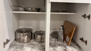 Et køkken med et hvidt skab, en marmor bordplade og rustfrit stål-kogegrej.