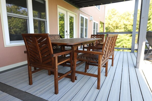A wooden deck with a table and chairs, a covered area with a roof, and a view of a building with windows.