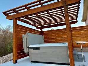 Un espacio de estar al aire libre cubierto con un banco y una mesa, listones de madera y barandilla de metal.