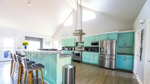 Una cucina moderna con mobili color petrolio, elettrodomestici in acciaio inossidabile e un'isola centrale con sgabelli da bar.
