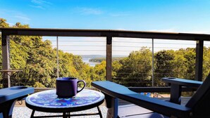 Un balcone con tavolo e sedie, una tazza blu e vista su alberi e un paesaggio lontano.