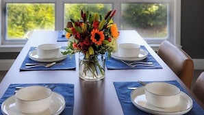 Un tavolo da pranzo apparecchiato con piatti e ciotole bianche, un vaso con fiori e un lampadario.
