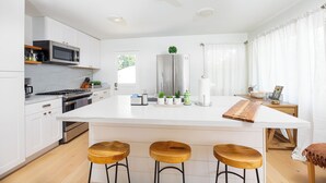 Une cuisine moderne avec des meubles blancs, des appareils en acier inoxydable, un grand îlot central doté de tabourets et une vue sur l’extérieur.