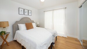 Une chambre à coucher avec un lit, une table de chevet, une lampe et une fenêtre avec des rideaux.