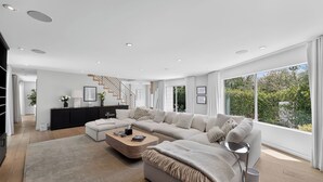 A modern living room with a large sectional sofa, a coffee table, and a staircase leading to an upper level. - Luxury Hollywood Hills Home With Pool, Outdoor Dining & Iconic Views Skyline Chalet (West Hollywood)