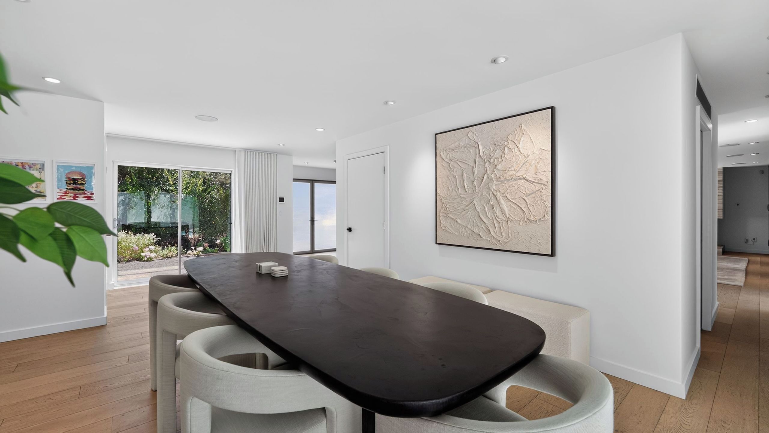 A modern dining area with a dark table, white chairs, and a large abstract painting on the wall.