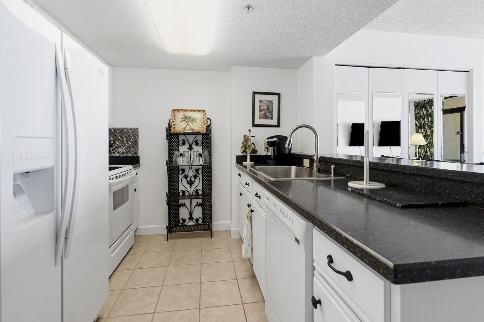 Una cocina moderna con armarios blancos, encimera negra, horno empotrado, lavamanos y una estantería metálica decorativa.