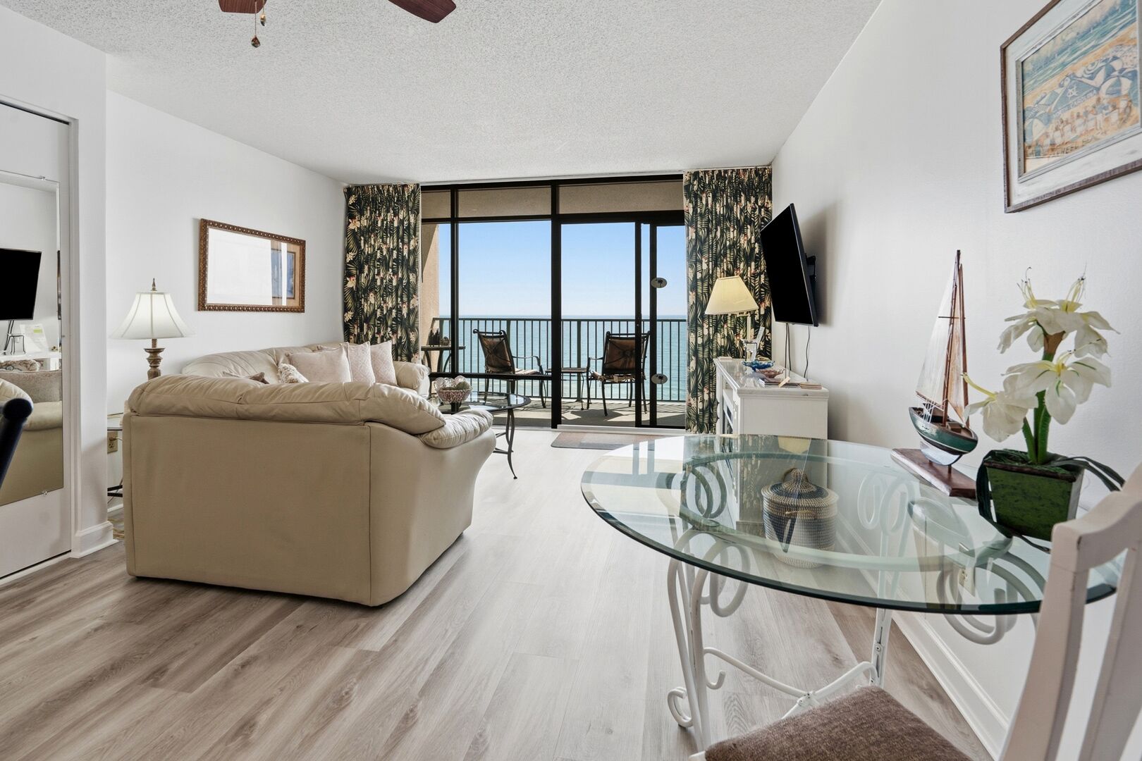 Un salón con sofá, una mesa de cristal, televisión y balcón con vistas.