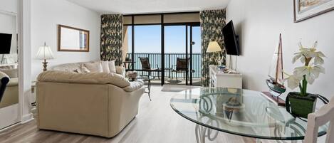 Un salón con sofá, una mesa de cristal, televisión y balcón con vistas.