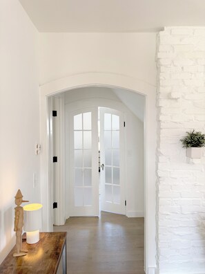 A hallway with white walls, a wooden floor, and a white brick accent wall. - Ptown Pearl · Central Location w/ Porch & Deck · Walk to Beach, Galleries & Town (Provincetown)