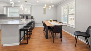 Een moderne keuken met een centraal kookeiland, barkrukken en een eethoek met een houten tafel en stoelen.