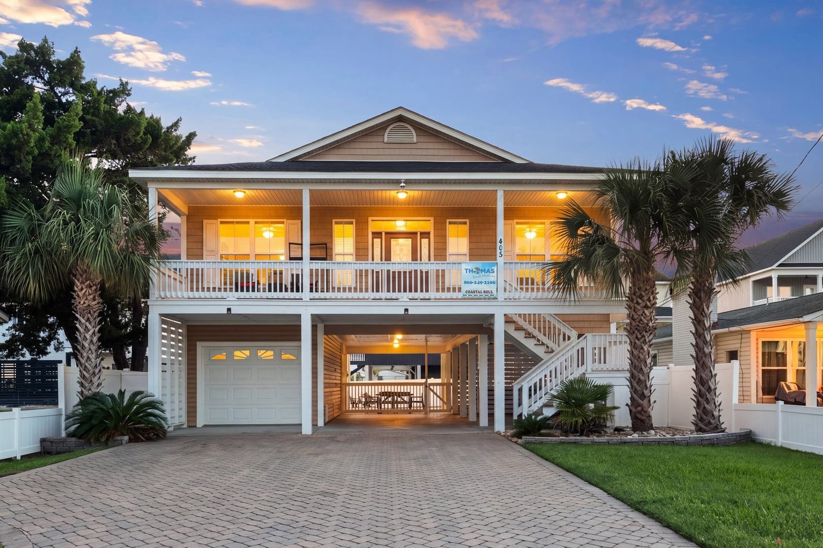 A two-story house with a covered front porch, a garage, and a sign indicating a coastal location.