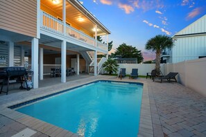 Una piscina con un porche cubierto, mobiliario exterior y una escalera que lleva a una terraza superior.