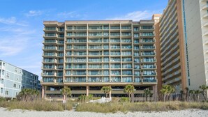 A multi-story hotel with balconies, located on a beach with palm trees. - Oceanfront 4BR condo with stunning views, balcony, pool & beach access in North Myrtle Beach (North Myrtle Beach)
