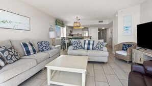 A modern living room with a grey sofa set, a white coffee table, and a wicker chair. A television is on a wooden stand to the right. - Oceanfront 4BR condo with stunning views, balcony, pool & beach access in North Myrtle Beach (North Myrtle Beach)
