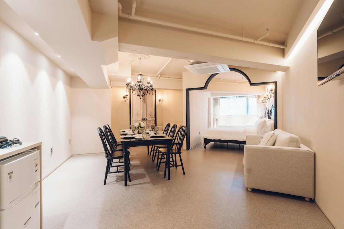 A modern, well-lit dining area with a chandelier, a sofa, and a bed in the background.